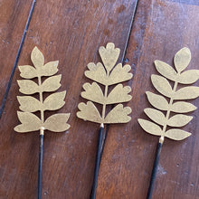 Load image into Gallery viewer, gold metal color plant pick. The top is shaped like leaves on a branch. the bottom is black and is meant to be added to floral decor or a houseplant
